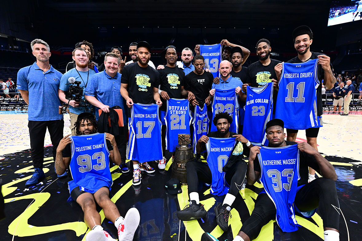 Team and staff on court after a championship game, holding commemorative jerseys